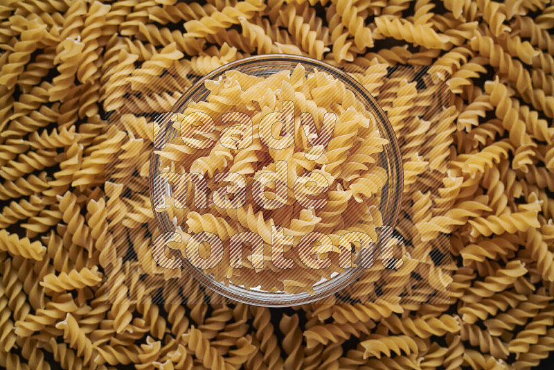 Fusilli pasta in a glass bowl on black background