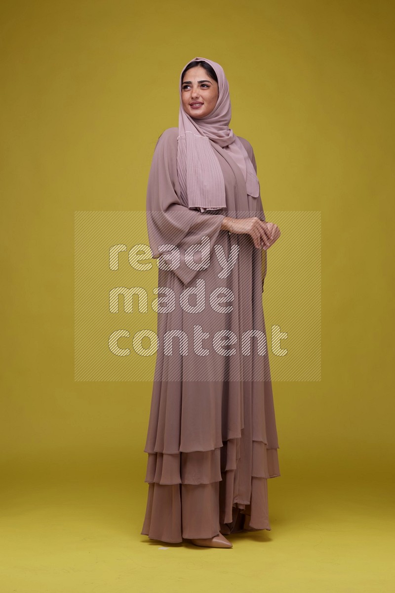 A woman Posing on a Yellow Background wearing Brown Abaya with Hijab