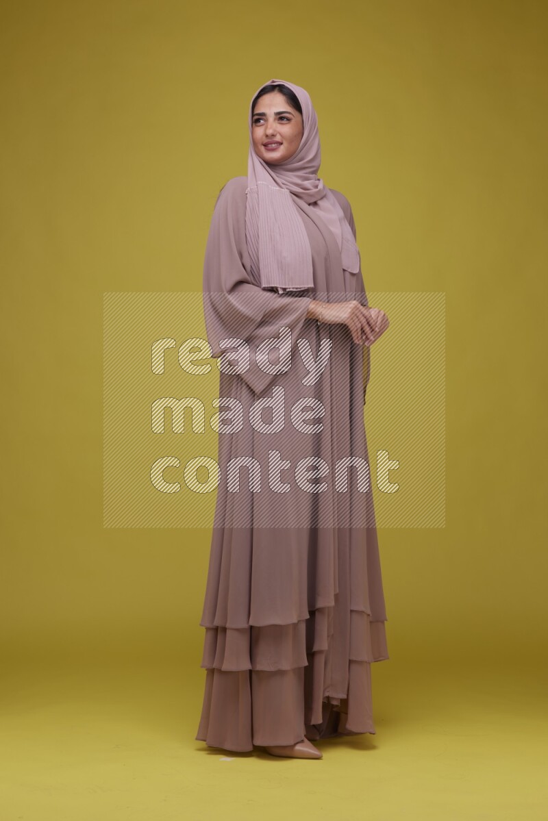 A woman Posing on a Yellow Background wearing Brown Abaya with Hijab