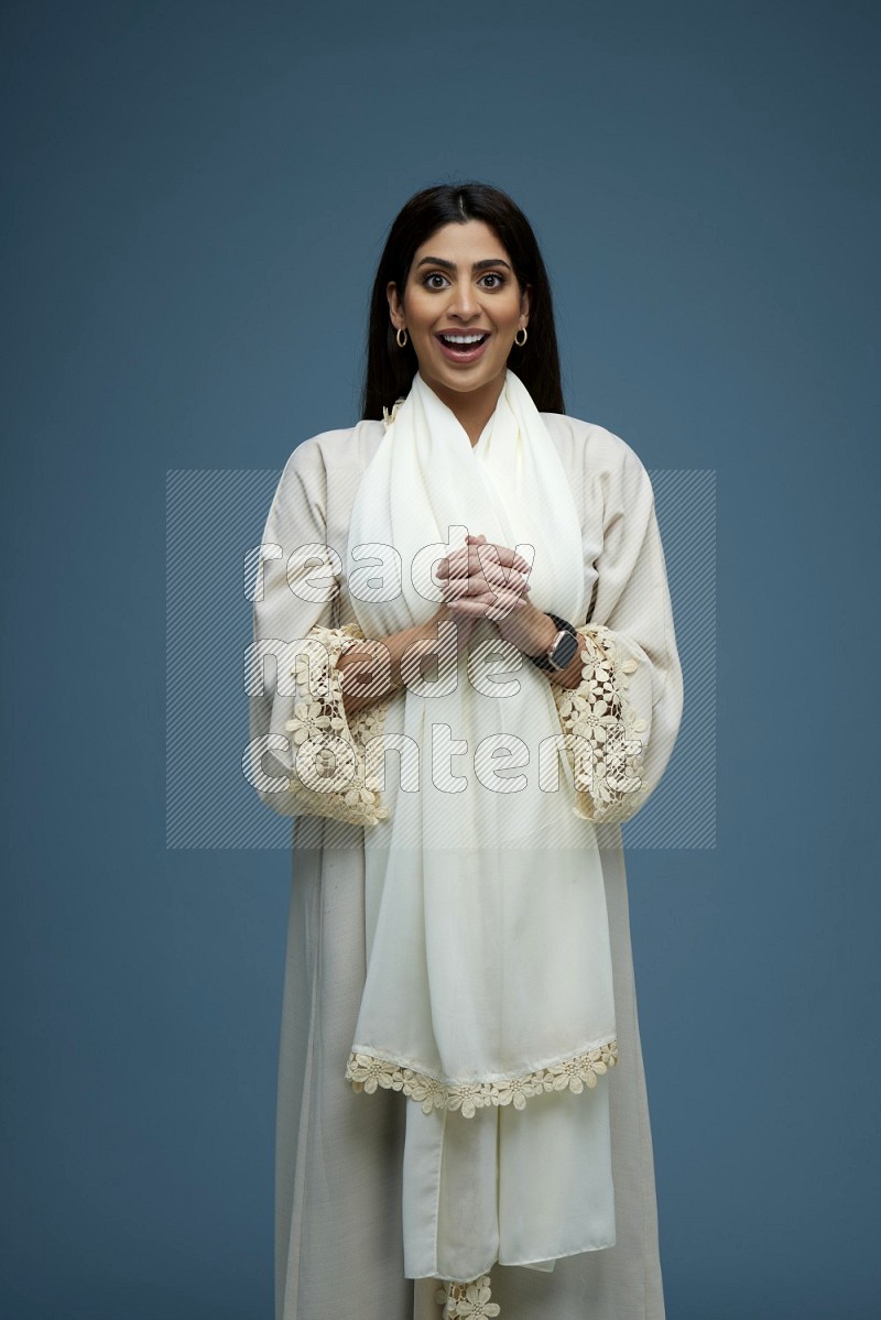 A Saudi woman posing in a blue background wearing an off-white Abaya no Hijab