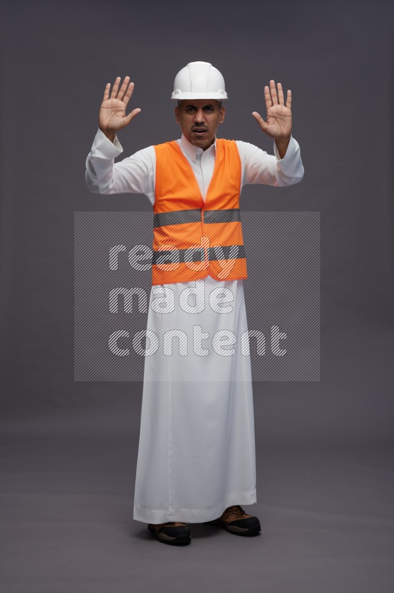 Saudi man wearing thob with engineer vest standing interacting with the camera on gray background