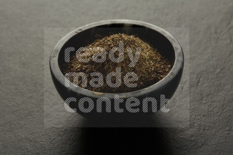 black pottery round sauce bowl filled with herbs on grey textured countertop