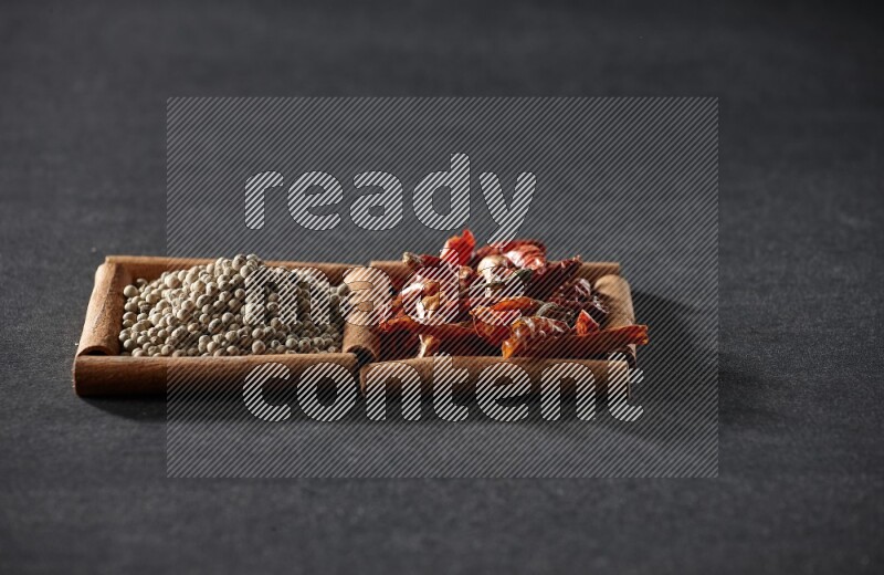 مربعان من أعواد القرفة ممتلئان بالفلفل الحار المجفف وحبوب الفلفل الأبيض علي خلفية سوداء