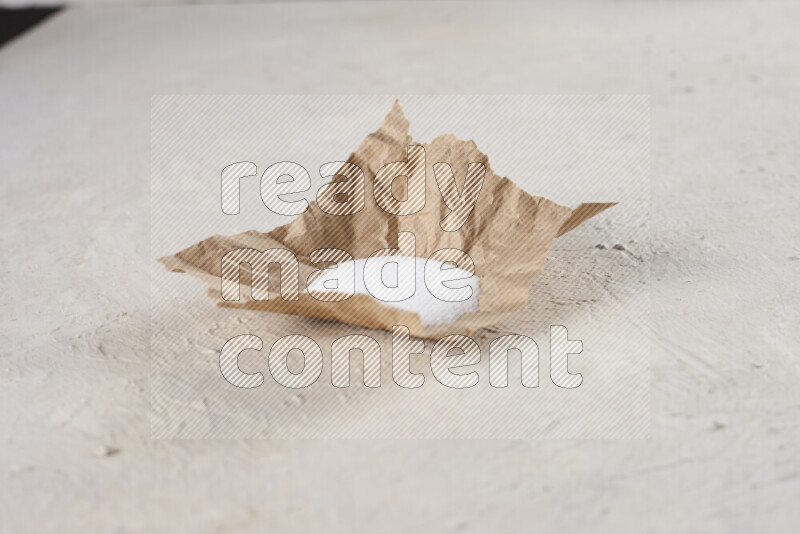 A crumpled piece of paper full of white salt on white background