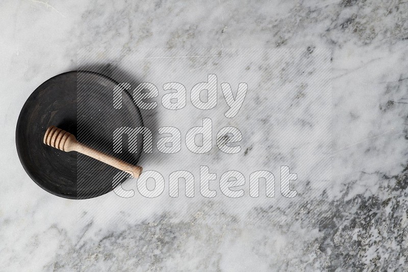 Black Pottery Plate with wooden honey handle in it, on grey marble flooring, Top View