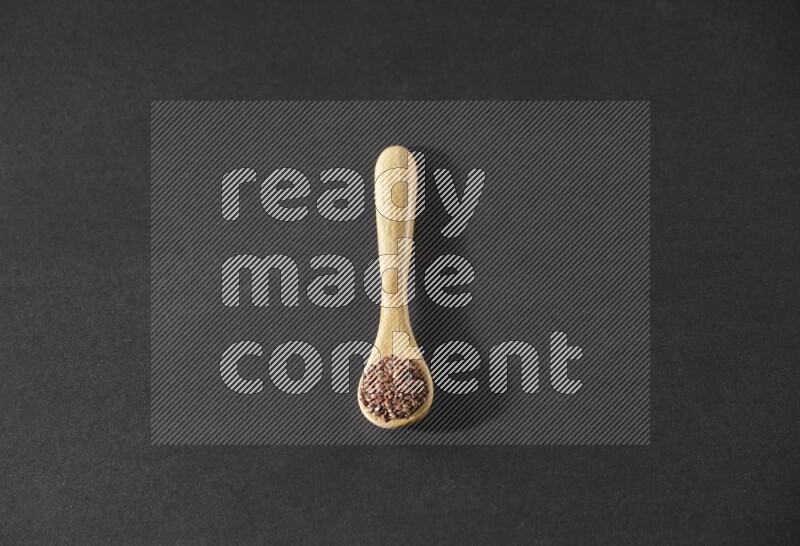 ملعقة خشبية ممتلئة بحبوب بذر الكتان علي خلفية سوداء