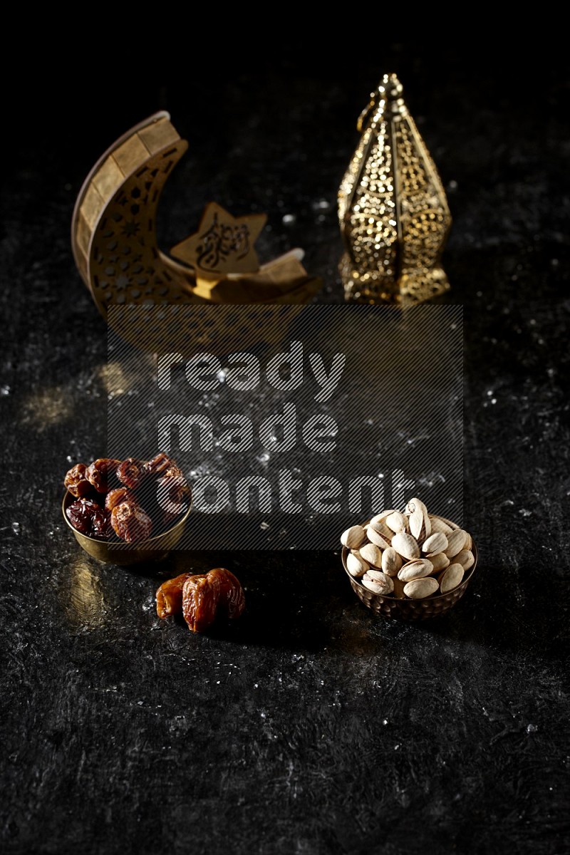 Dates in a metal bowl with pistachios beside golden lanterns in a dark setup