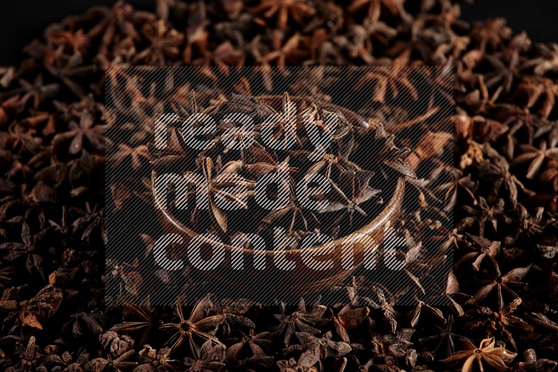 Star Anise in a wooden bowl and surrounded by more anise filling the frame on black flooring