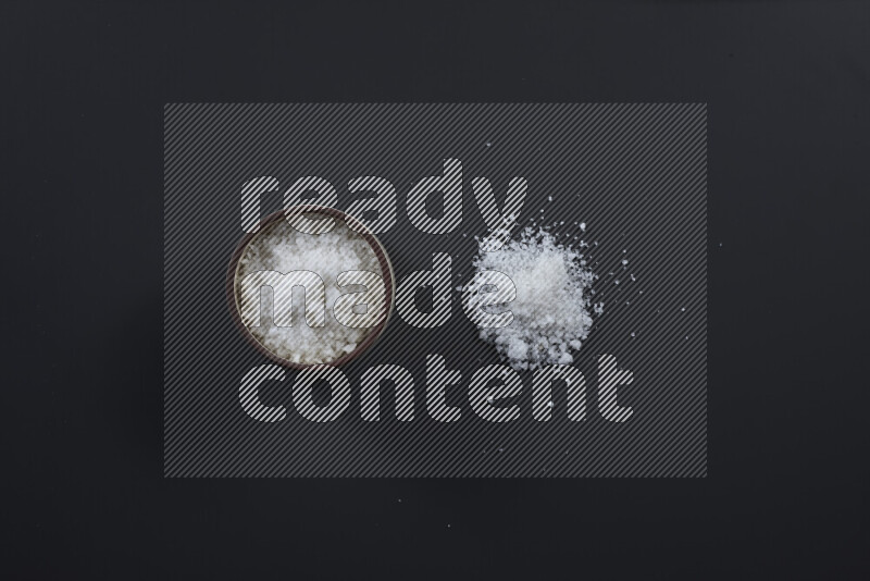 Pottery bowl full of fine table salt and coarse sea salt on black background
