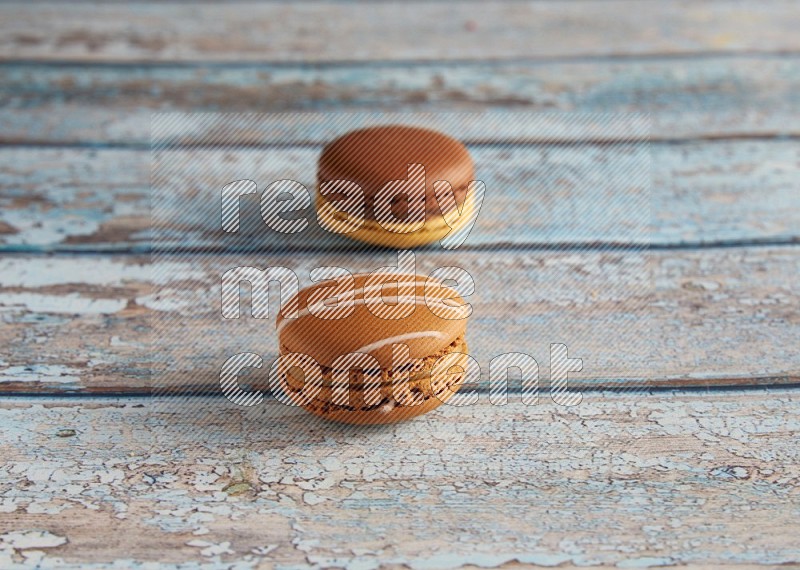 45º Shot of of two assorted Brown Irish Cream, and Yellow, and Brown Chai Latte macarons  on light blue background