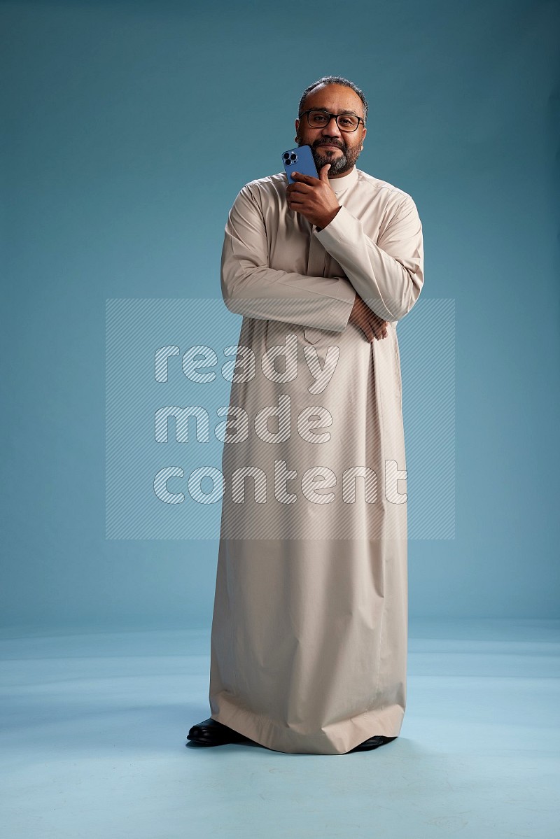 Saudi Man without shimag Standing texting on phone on blue background