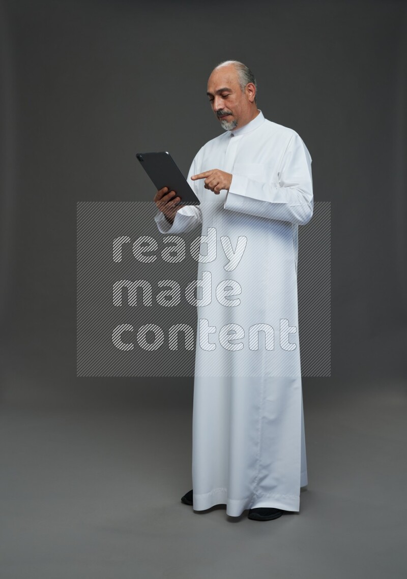 Saudi man without shomag Standing working on tablet on gray background