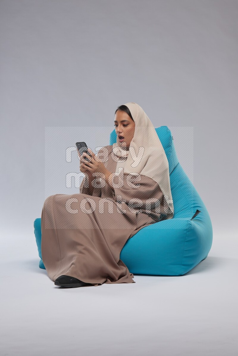 A Saudi woman sitting on a blue beanbag and texting on phone