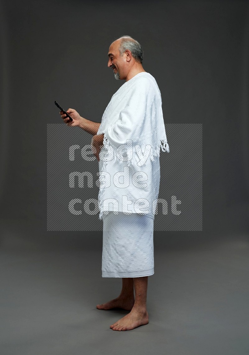 A man wearing Ehram Standing texting on phone on gray background