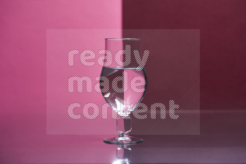 The image features a clear glassware filled with water, set against pink and dark red background