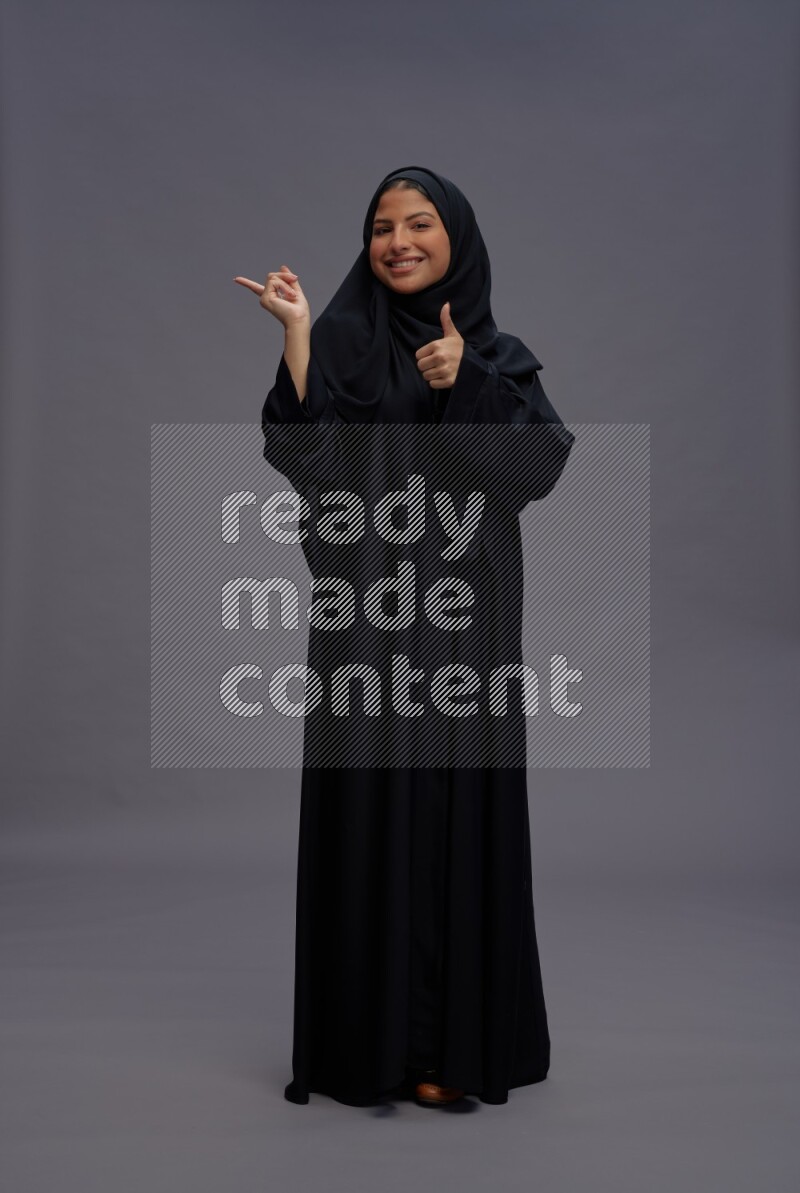 Saudi woman wearing Abaya standing interacting with the camera on gray background