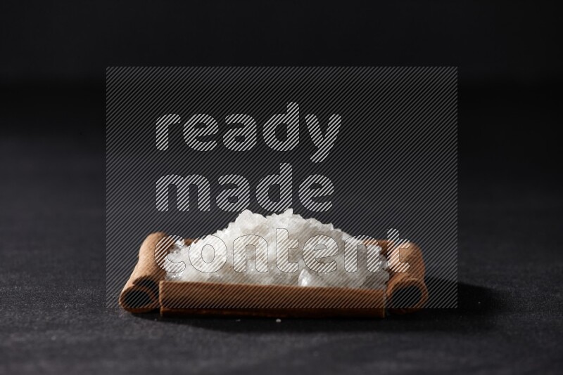 أربعة من أعواد القرفة مكونة شكل مربع بداخلها ملح أبيض علي خلفية سوداء