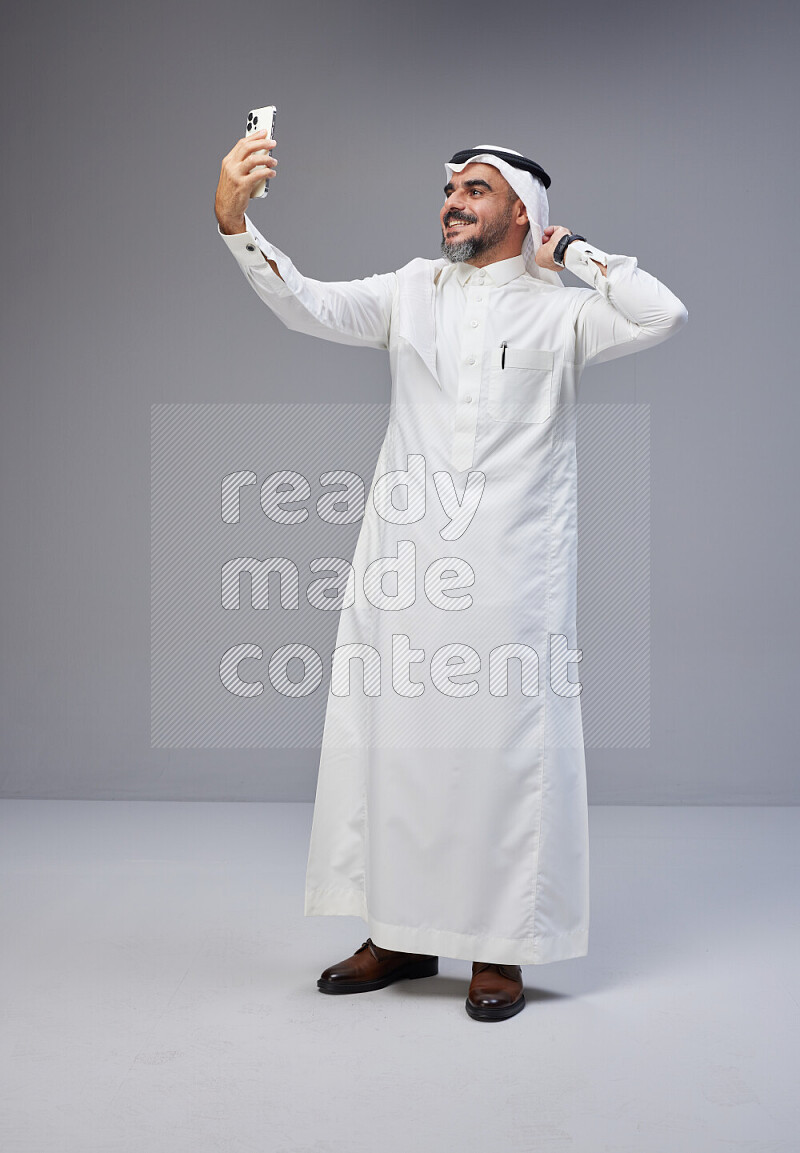 رجل سعودي يرتدي ثوب وشماغ ابيض يلتقط سلفي بجواله