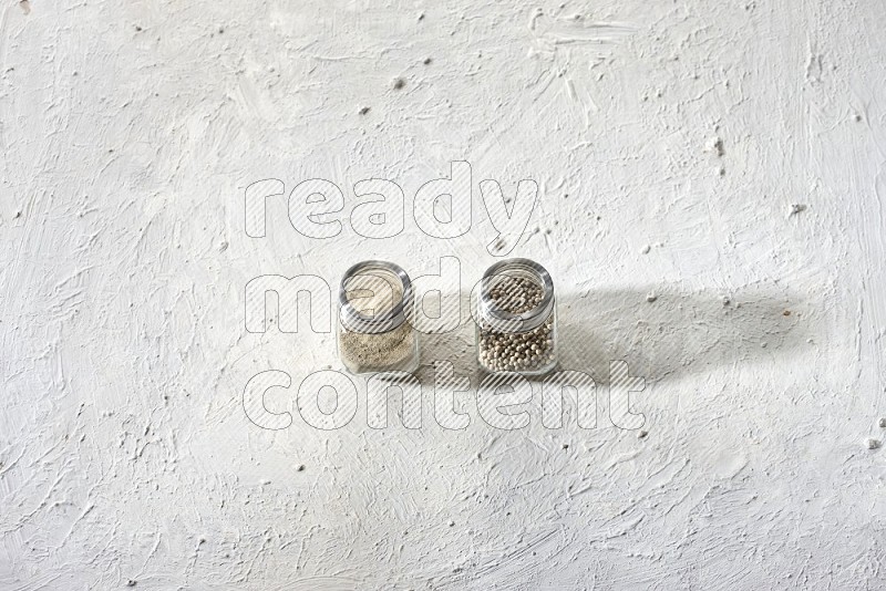 2 Herbal Glass jar full of white pepper beads and powder on textured white flooring