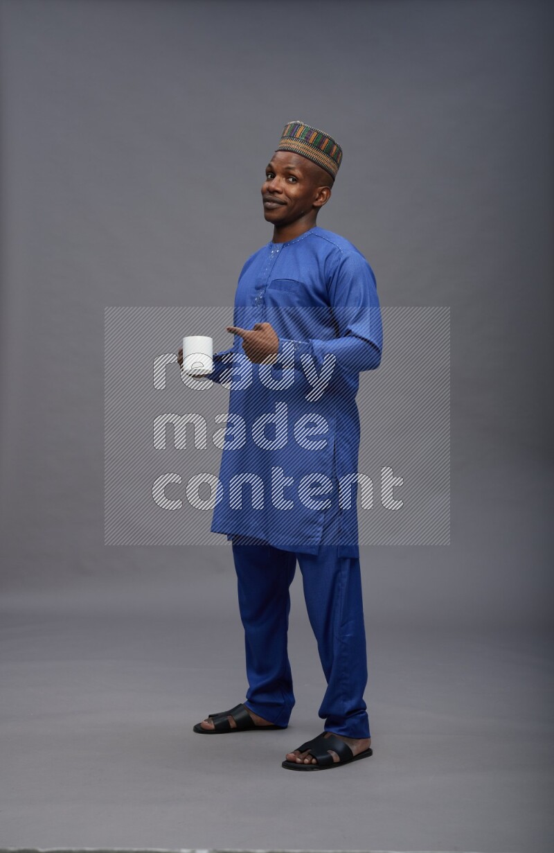 Man wearing Nigerian outfit standing holding mug on gray background