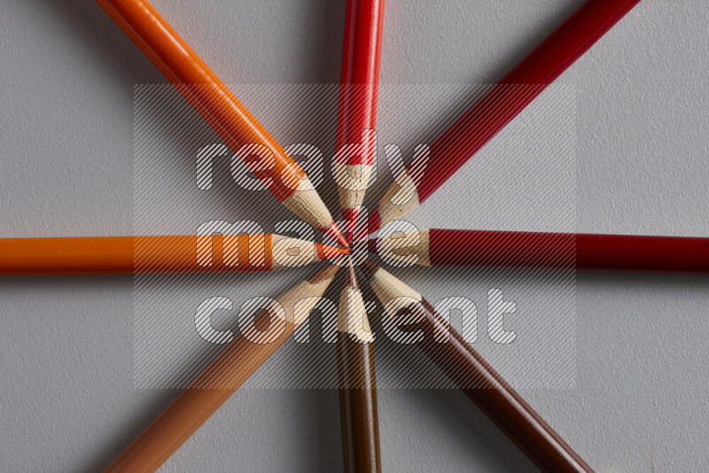 مجموعة من الأقلام الخشبية الملونة بتدرجات اللون البرتقالي والأحمر على خلفية رمادية