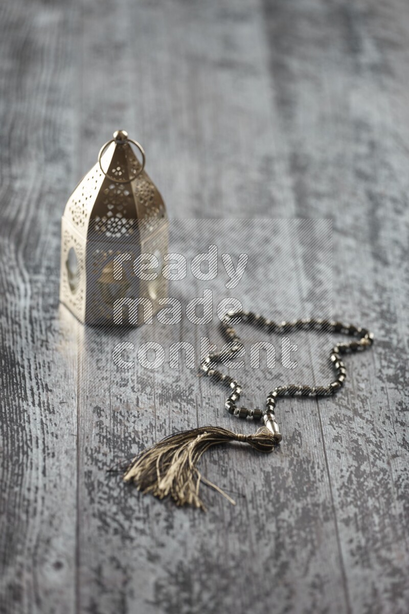 A silver lantern with different drinks, dates, nuts, prayer beads and quran on grey wooden background