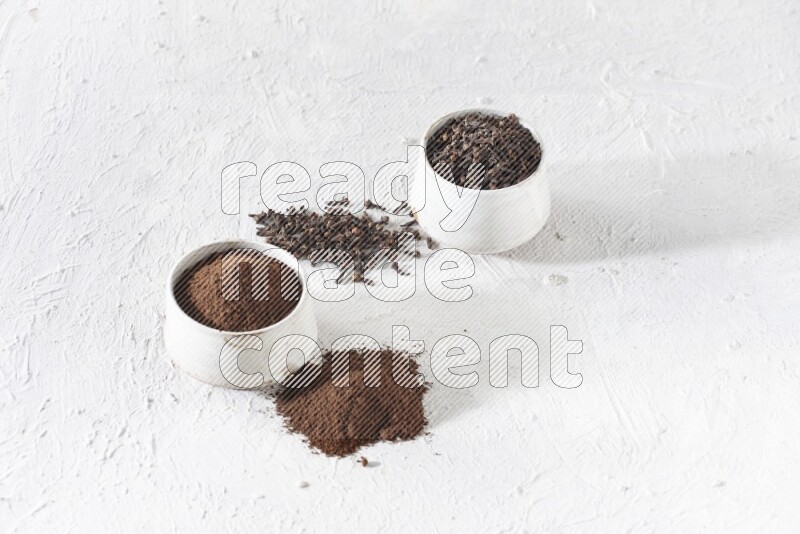 2 Beige ceramic bowls, one full of cloves and the other full of powder on textured white flooring