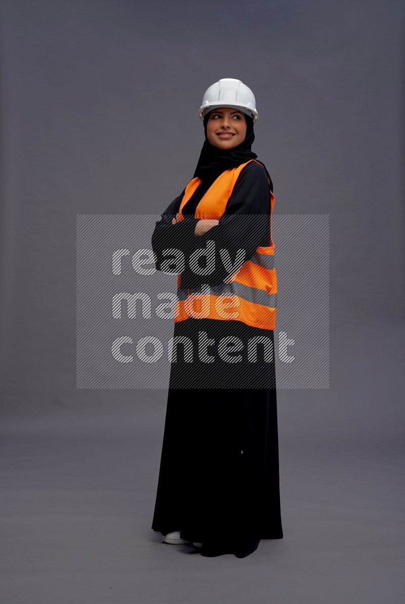 Saudi woman wearing Abaya with engineer vest standing with crossed arms on gray background