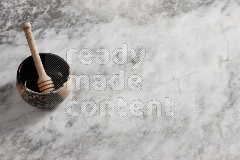 Multicolored pottery bowl with wooden honey dipper in it on grey marble background