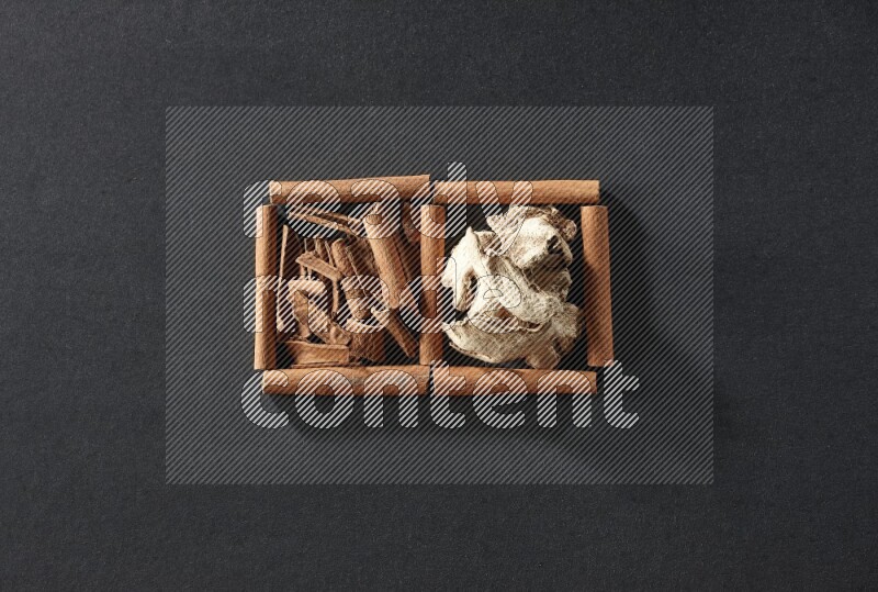 مربعان من أعواد القرفة ممتلئان بقطع من القرفة والزنجبيل المجفف علي خلفية سوداء