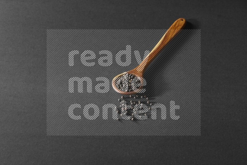 حبوب الفلفل الأسود في مغرفة خشبية علي خلفية سوداء