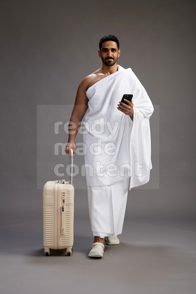 A man wearing Ehram Standing holding traveling bag on gray background