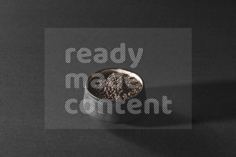 A black pottery bowl full of black pepper beads on black flooring