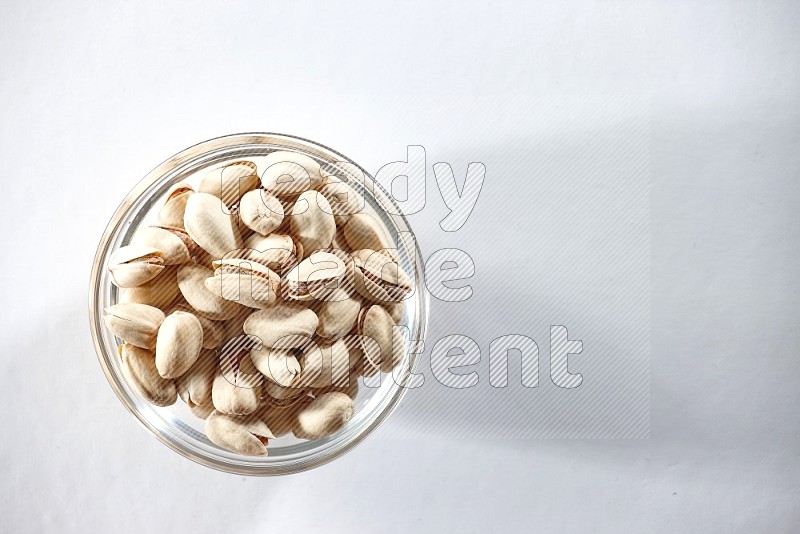 A glass bowl full of pistachios on a white background in different angles