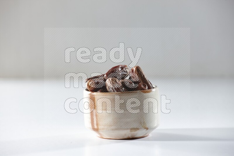 A beige ceramic bowl full of dried dates on a white background in different angles