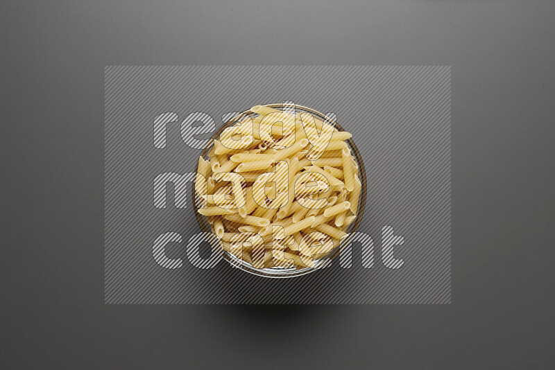 Mini penne pasta in a glass bowl on grey background