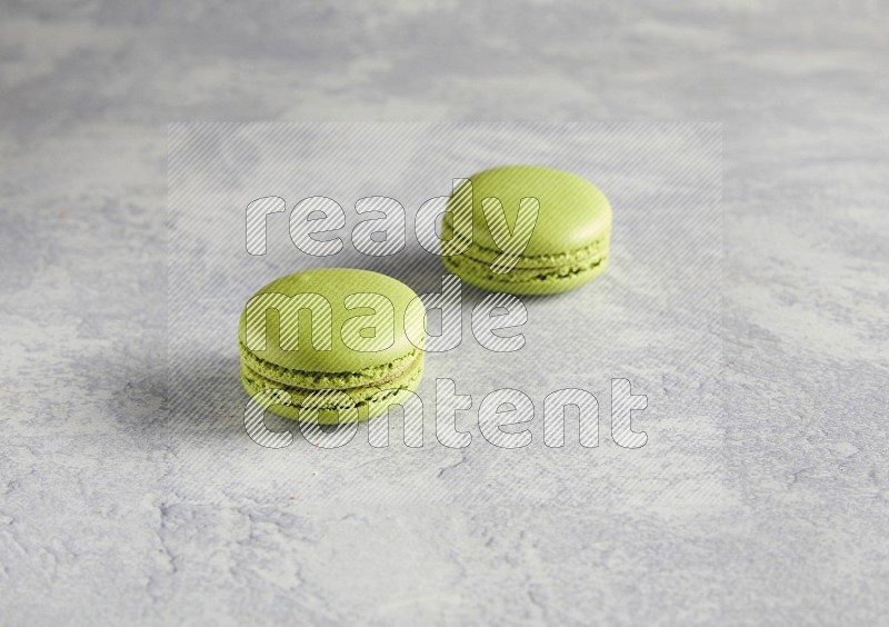 45º Shot of two Green Pistachio macarons  on white  marble background