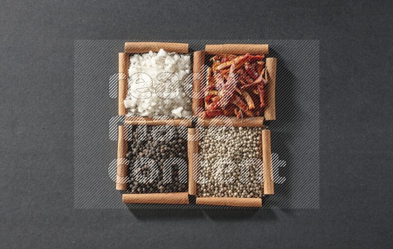 4 مربعات من عيدان القرفة ممتلئة بحبوب الفلفل الأسود والفلفل الأبيض والفلفل الحار والملح الأبيض على أرضية سوداء