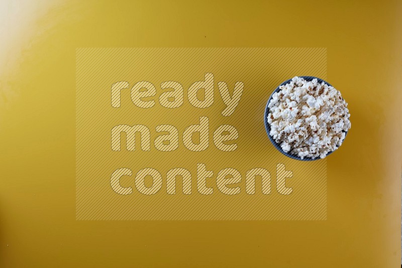 A blue pottery bowl full of popcorn on a yellow background in different angles