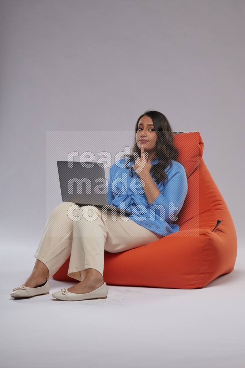 A woman sitting on an orange beanbag and working on laptop