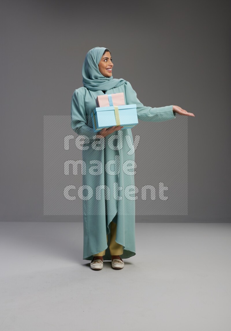Saudi Woman wearing Abaya standing holding gift box on Gray background