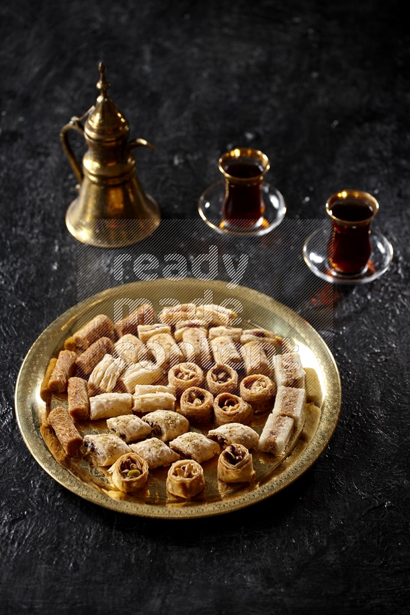حلويات شرقية مع الشاي وإبريق معدني علي خلفية سوداء خشبية