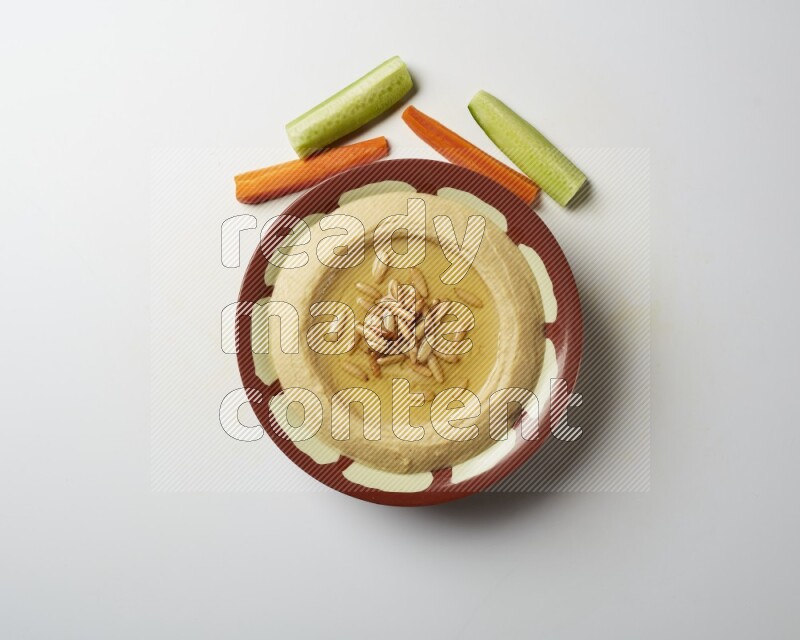 Hummus in a traditional plate garnished with pine nuts on a white background