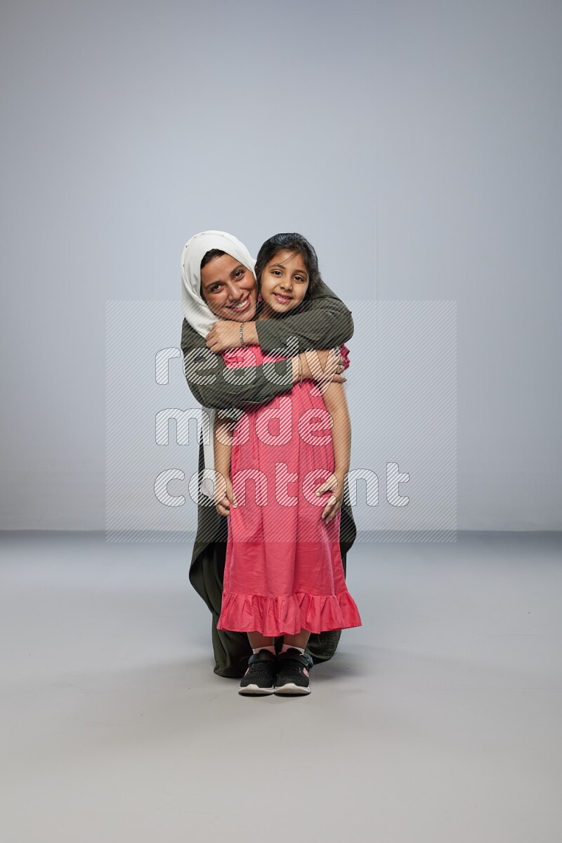A girl and her mother interacting with the camera on gray background