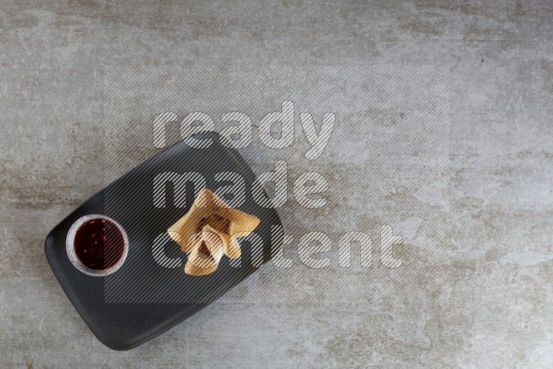 wonton cups with soy sauce ramkin on rectangle dark grey ceramic plate on grey textured counter top