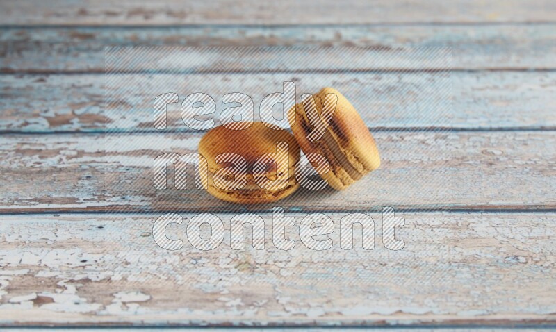 45º Shot of two Yellow Crème Brulée macarons on light blue wooden background