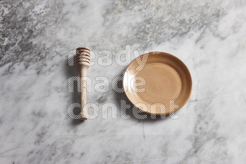Beige pottery plate with wooden honey dipper on the side on grey marble background