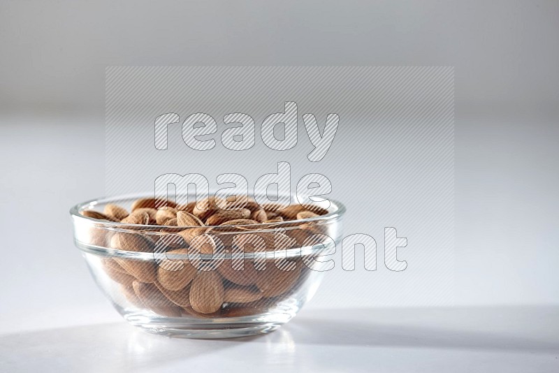 A glass bowl full of peeled almonds on a white background in different angles