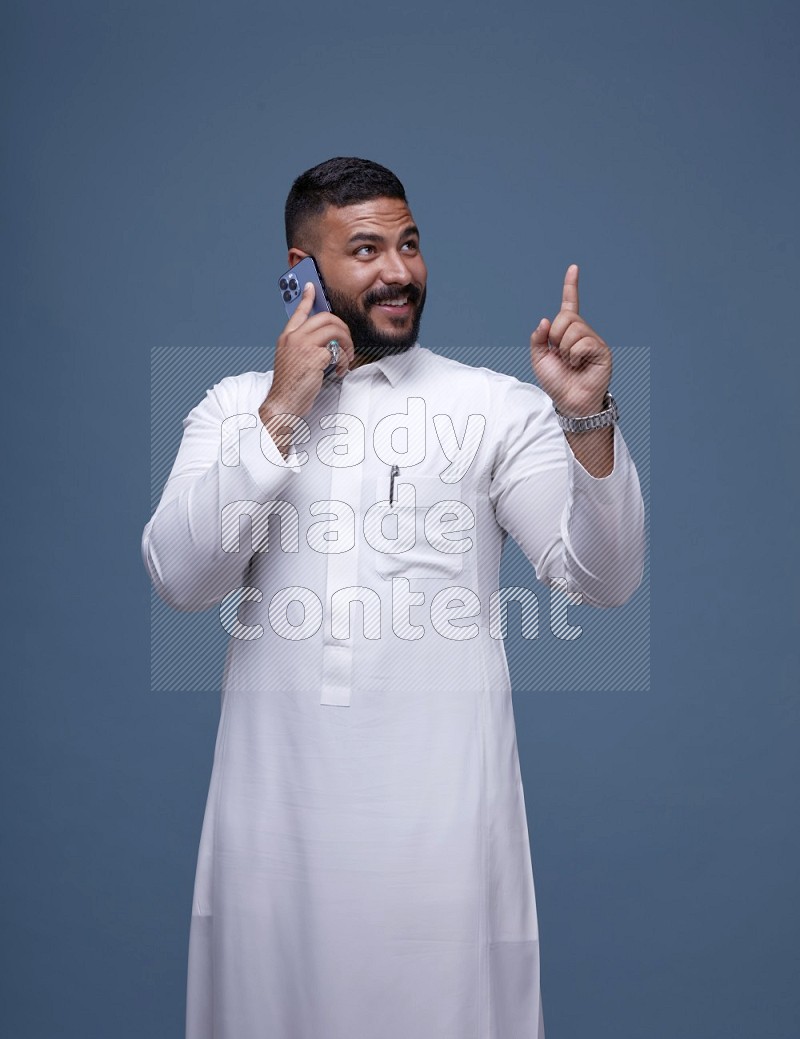 A Saudi man calling on blue background wearing Saudi Thob