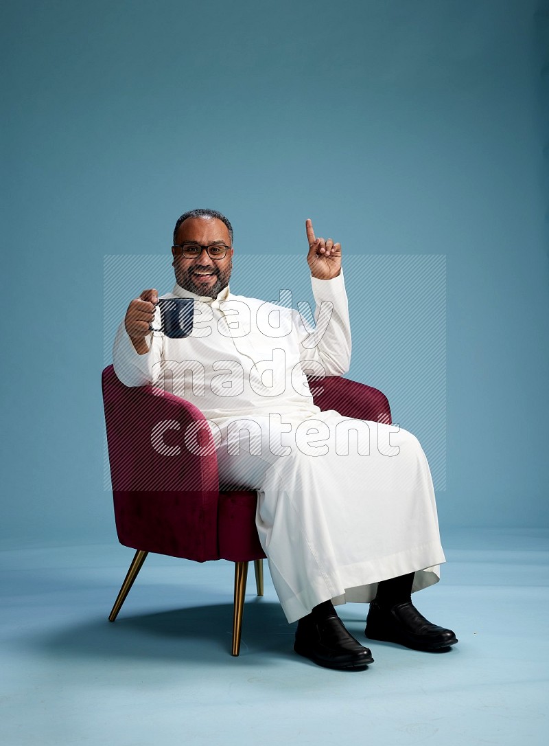 Saudi Man without shimag sitting on chair drinking coffee on blue background